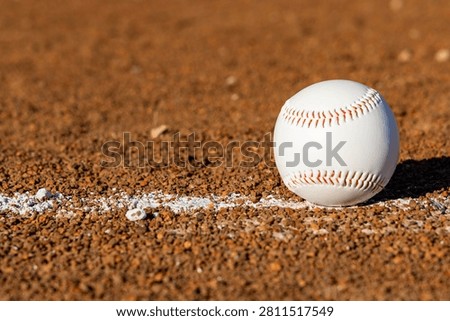 Close-up view of a baseball on a baseball field's dirt infield, with a white foul line marking the boundary