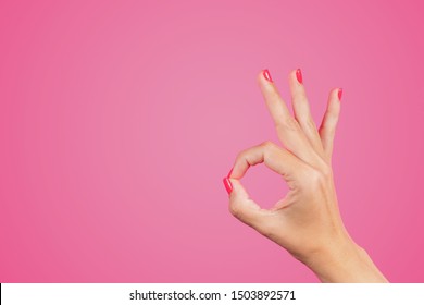 Closeup view of beautiful white female hand isolated on pink background. WOman making ok gesture with rounded fingers. Horizontal color photography.
