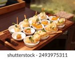 A close-up view of a beautifully arranged assortment of gourmet appetizers served in small white bowls on a wooden tray. The appetizers are elegantly garnished with microgreens.