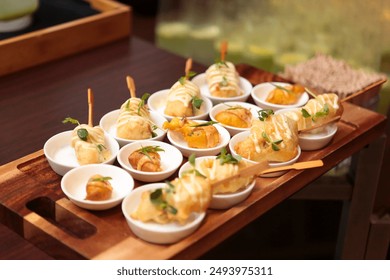 A close-up view of a beautifully arranged assortment of gourmet appetizers served in small white bowls on a wooden tray. The appetizers are elegantly garnished with microgreens. - Powered by Shutterstock