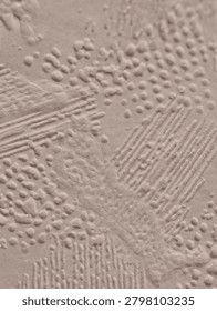 Close-up view of a beige plaster surface featuring decorative trowel strokes, linear ridges and clusters of raised dot patterns. Soft directional lighting emphasizes the relief