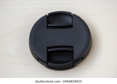 Close-up view of a black camera lens cap without logo on wooden background. A lens cover or lens cap protects camera lenses from scratches, dust, rain, snow, minor collisions, and oily residue. - Powered by Shutterstock