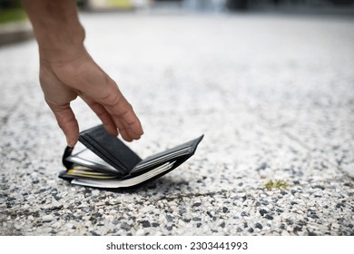 Closeup view of black man picking up lost wallet full of money banknotes on city street, selective focus, empty space. Lost money concept - Shutterstock ID 2303441993