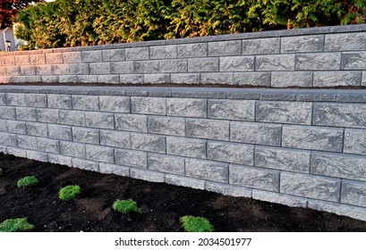 A Closeup View Of Block Shape Retaining Wall Built As A Two Tier Wall Into An Existing Garden Landscape With A Hedge On Top Of The Hill.