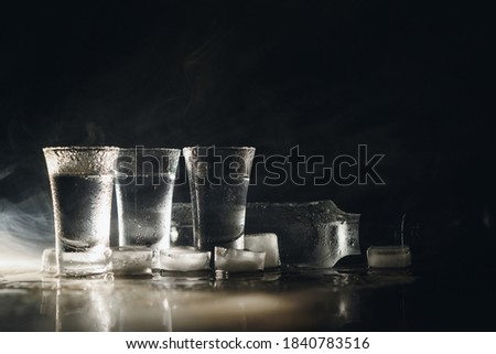 Close-up view of bottle of vodka with glasses standing on ice on black