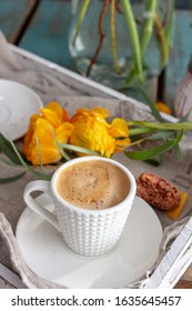 Closeup View Of A Breakfast Concept With A Cup Of Coffee At The Front, A Piece Of Macaroon Beside The Coffee Dish And A Pair Of Buttercup Flower Laying On The Table.