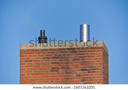 A close-up view of a brick chimney with two different types of chimney caps against a clear blue sky.