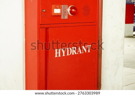 A close-up view of a bright red fire hydrant cabinet installed on a white wall in a parking structure, featuring an alarm light and emergency controls.