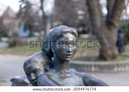 Close-up view of bronze woman sculpture with a child at her back in the park