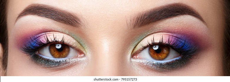 Closeup view of brown female eyes with evening makeup. Colorful pink and blue smokey eyes. Studio shot