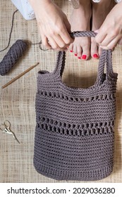 Closeup View Of A Brown Summer Chain Stitch Crochet Bag Held By A White Woman On A Burlap Floor.