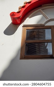 A close-up view of a building facade featuring a vibrant red decorative element above a simple wooden window reflecting the sky and surrounding structures