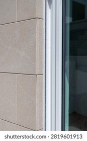 Close-up view of a building facade featuring beige stone cladding adjacent to a white window frame and reflective glass