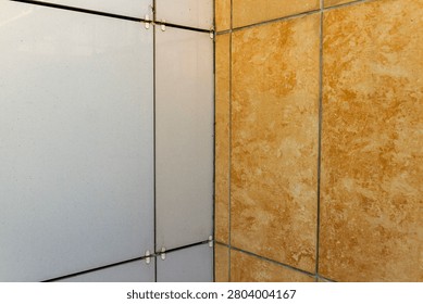 Close-up view of building facade installation showing contrasting white composite panels and orange marble texture porcelain tiles.