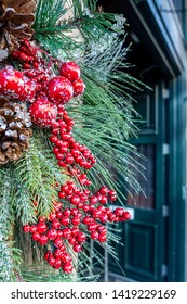Close-up View Of A Bunch Of Hanging Christmas Decorations Outside A Doorway, Consisting Of Artificial Red Mistletoe Berries, Pine Cones And Leaves, With A Sprinkling Of Artificial Snow.