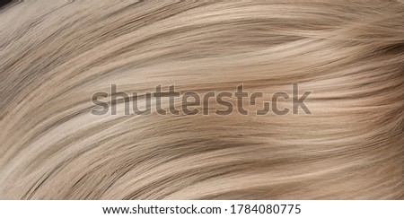 A closeup view of a bunch of shiny straight blond hair in a wavy curved style.