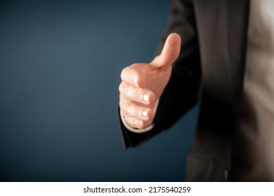 Closeup view of a businessman offering his hand in handshake or greeting over blue background. With copy space on the left side of the image. - Powered by Shutterstock