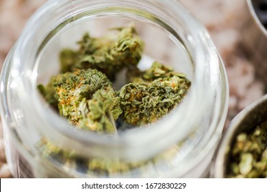 Close-up view of cannabis buds in a glass jar. Buds are fresh, dry, and look healthy. A large amount of THC crystals can be seen on the buds.