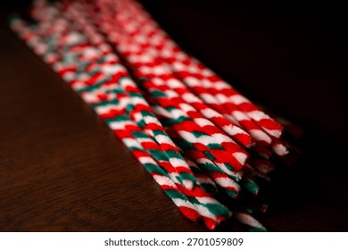 A close-up view captures a bundle of red, green, and white striped pipe cleaners resting diagonally on a dark wooden surface.