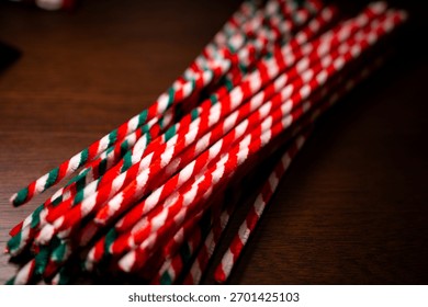 A close-up view captures a bundle of red, green, and white striped pipe cleaners resting diagonally on a dark wooden surface.