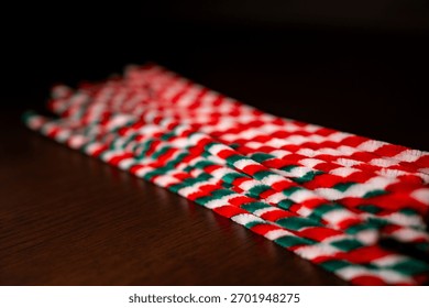 A close-up view captures a bundle of red, green, and white striped pipe cleaners resting diagonally on a dark wooden surface.