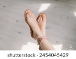 A close-up view captures a womans feet crossed at the ankles, adorned with delicate pale pink sandals.