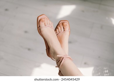A close-up view captures a womans feet crossed at the ankles, adorned with delicate pale pink sandals. - Powered by Shutterstock