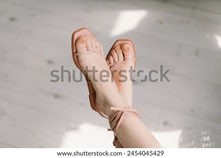 A close-up view captures a womans feet crossed at the ankles, adorned with delicate pale pink sandals.