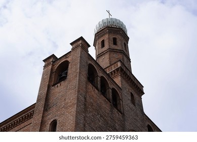 A close-up view capturing the intricate brickwork and the distinctive onion dome of the Church of Saints Peter and Paul on Nikolskoe (St. Peter und Paul auf Nikolskoe) in Berlin-Wannsee. The photograph emphasizes the detailed geometric patterns and textures of the light and dark red bricks used in its construction between 1834 and 1837. The prominent onion dome, clad in patinated copper, is topped with a golden cross and features ornate decorations, showcasing the significant influence of Russian Orthodox architecture.