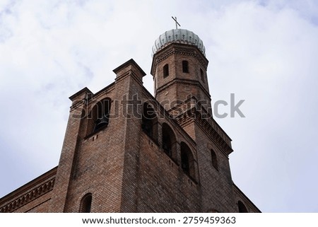 A close-up view capturing the intricate brickwork and the distinctive onion dome of the Church of Saints Peter and Paul on Nikolskoe (St. Peter und Paul auf Nikolskoe) in Berlin-Wannsee. The photograph emphasizes the detailed geometric patterns and textures of the light and dark red bricks used in its construction between 1834 and 1837. The prominent onion dome, clad in patinated copper, is topped with a golden cross and features ornate decorations, showcasing the significant influence of Russian Orthodox architecture.