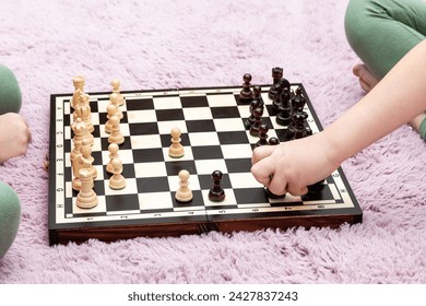 Close-up view capturing a young childs hand moving a chess piece during a game, with a focus on the black and white checkered board surrounded by various chess figures, intense competition gameplay
