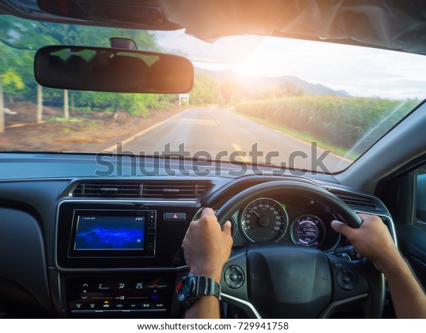 Close-up view from the car driving. Hands of a\
driver on steering wheel of a car and asphalt road. Journey on the\
road with speed