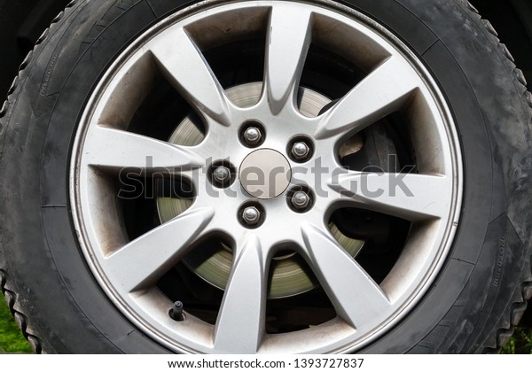 A closeup view of a car wheel with\
winter tires, silver brake disc and a five-nut\
rim