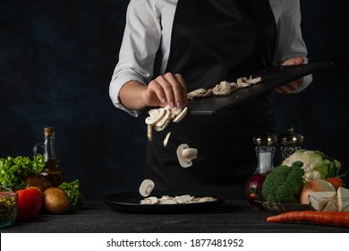 Close-up view of chef in black apron pours chopped mushrooms on the plate for cooking soup on dark blue background. Backstage of preparing meal. Healthy dish. Food concept. Frozen motion. Cookbook. - Powered by Shutterstock