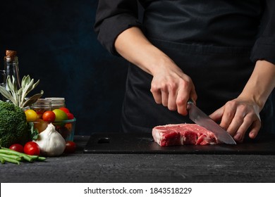 Close-up view of chef cuts with knife raw steak on wooden chopped board. Backstage of preparing grilled pork meat at restaurant or hotel.