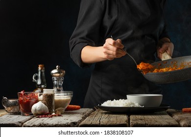 Close-up View Of Chef Pours By Ladle Chicken Curry From Pan Wok To White Bowl. Backstage Of Serving Traditional Indian Curry With Boiled Rice On Black Background. Concept Of Cooking Tasty Hot Meal.