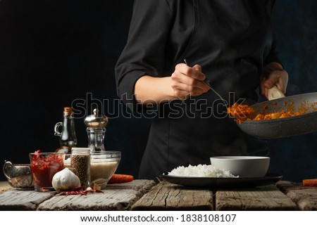 Close-up view of chef pours by ladle chicken curry from pan wok to white bowl. Backstage of serving traditional Indian curry with boiled rice on black background. Concept of cooking tasty hot meal.
