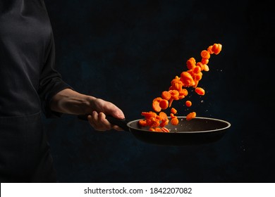 Close-up view of chef's hand throws up chopped carrot above the frying pan on dark blue background. Backstage of cooking meal. Frozen motion. Food banner concept. - Powered by Shutterstock