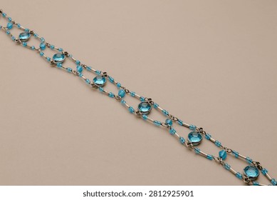 A close-up view of a chic blue beaded necklace, featuring light blue circular gems and delicate silver accents, presented against a neutral beige backdrop. The overall mood is sophisticated and elegant. This image is perfect for showcasing jewelry, fashion accessories, or gift ideas