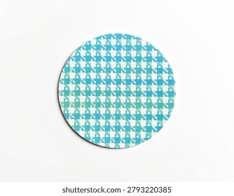A close-up view of a circular object featuring a repeating blue and green houndstooth pattern on a white background.