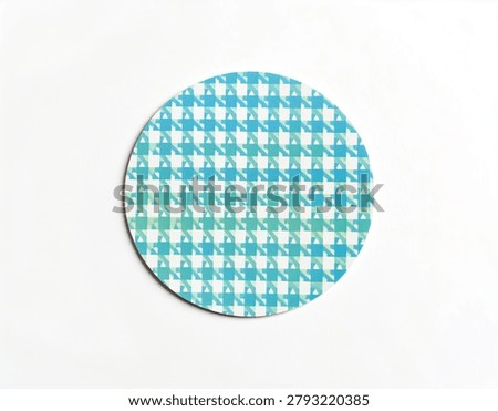 A close-up view of a circular object featuring a repeating blue and green houndstooth pattern on a white background.