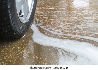 A Close-up View Of Civil Car Wheel In Soap Puddle On The Floor Of Washing Garage. Car Wash And Environmental Conservation Concept Picture.