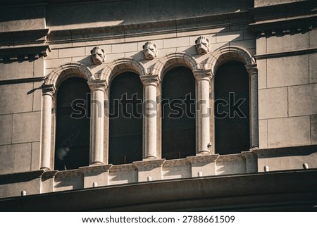 Close-up view of a classical building facade featuring arched windows framed by columns and adorned with grotesque carvings above