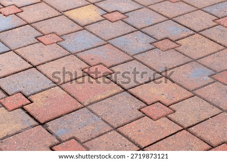 A close-up view of colorful interlocking paver tiles arranged in a red diamond pattern. Perfect for outdoor pathways, patios, and urban landscaping visuals, conveying order, texture and durable design