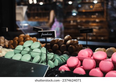 Close-up view of colorful macarons on display in a bakery, with labels ("raspberry" from French) indicating flavors. In the background, a blurred interior of the shop showcases more gourmet treats. - Powered by Shutterstock