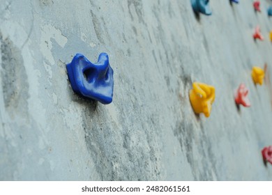 A closeup view of colorful plastic handholds attached to a concrete climbing wall. - Powered by Shutterstock