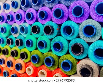 Close-up view of colorful thread spools arranged in rows at a textile manufacturing facility. Vibrant yarn cones in various colors create an attractive industrial pattern, representing textile production, fabric manufacturing, fashion industry, craftsmanship, and creative design concepts.