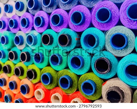 Close-up view of colorful thread spools arranged in rows at a textile manufacturing facility. Vibrant yarn cones in various colors create an attractive industrial pattern, representing textile production, fabric manufacturing, fashion industry, craftsmanship, and creative design concepts.