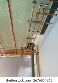 A close-up view of a complex network of copper plumbing and red electrical wiring against a concrete ceiling
