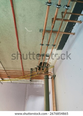 A close-up view of a complex network of copper plumbing and red electrical wiring against a concrete ceiling
